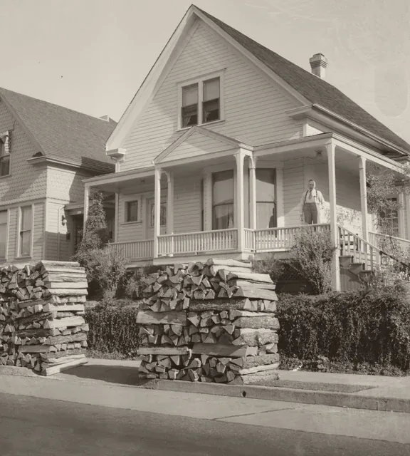 A homeowner on the porch of a Portland, Oregon house in 1939, firewood stacked at the curb. Photograph by Dorothea Lange.